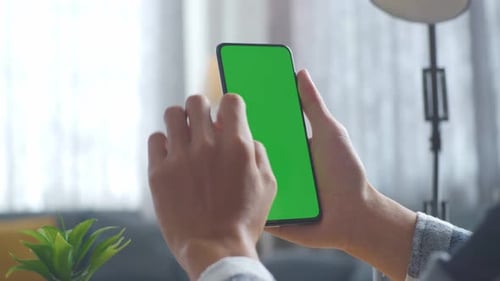 Close up of man's hands using a mock up green screen smartphone on a desk