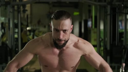 A Muscular Athlete with a Beard Does a Chest Exercise with the Help of Sports Equipment