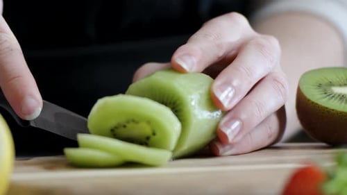 close up of slicing fresh kiwi fruit on wooden cutting board