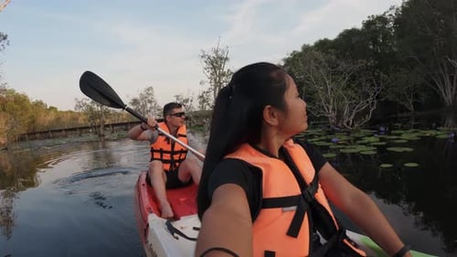 A thai woman is recording a selfie shot using an action camera while kayaking in a mangrove forest w