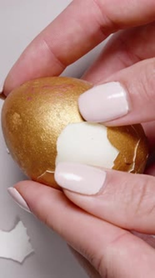 Vertical video. Close-up of hands removing the golden shell from a hard-boiled Easter egg, revealing