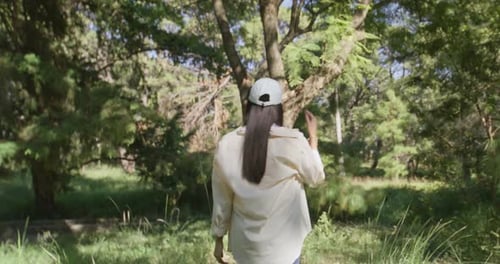 Woman Walking in Lush Green Forest Stretching Arms in Sunlight