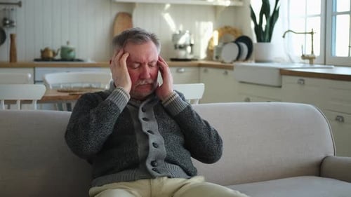 Man Massaging Temples While Sitting on Couch