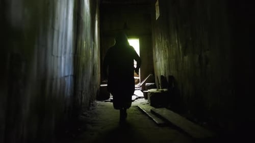Hooded Figure Walking Down a Dark Urban Tunnel