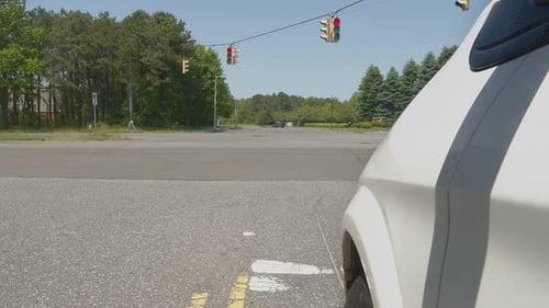White car pulls up to traffic light and stops, during the day, with driver's side of car and wheel i