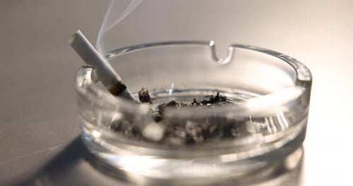 Ashtray with ash and smoldering cigarette butt on grey table, closeup