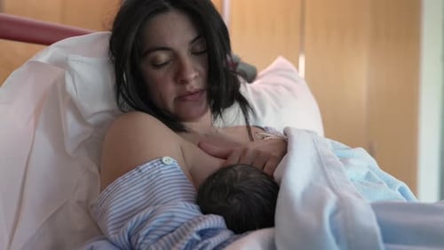 New mother struggles with breastfeeding pain after giving birth to baby seated at hospital bed,