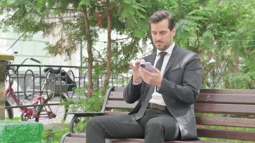 Man in Suit Uses Smartphone on Park Bench
