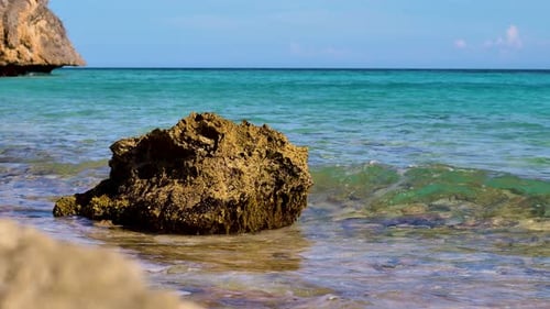 4k 60fps slow slider of rock getting hit by small waves in shallow water, tropical caribbean bay inl