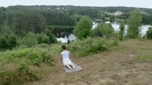 Man in Sportswear Does Yoga Pose on Mat on Green River Bank