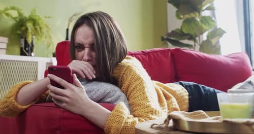 Woman Lying on Couch Uses Phone with Annoyance