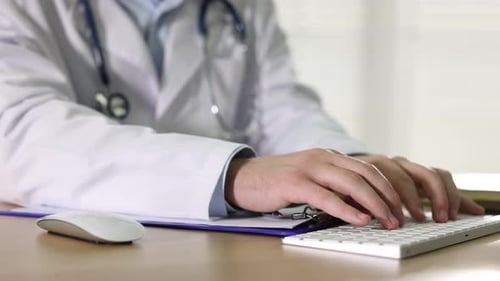 Doctor Typing on Keyboard and Writing on Chart