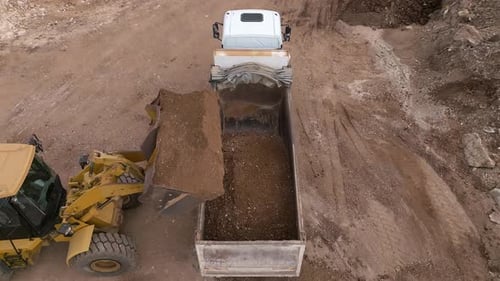 Bucket loader loading soil onto a truck trailer, Top down view