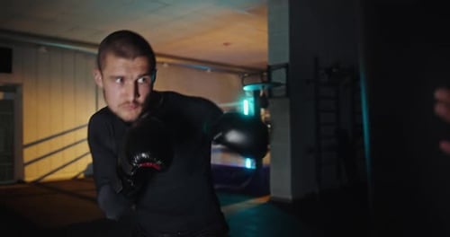 Young Professional Boxer Practicing Punches on Heavy Bag in Gym