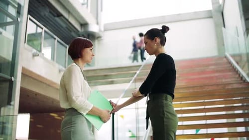Young businesswomen discussing a project near a modern office staircase