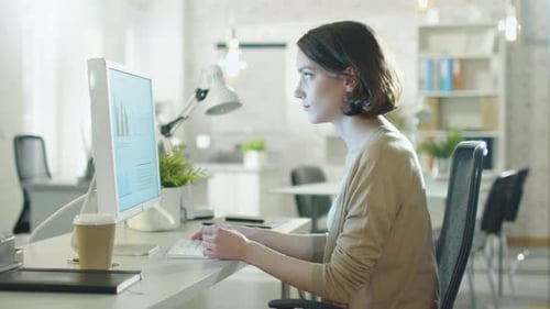 Young Beautiful Woman Works Sitting at Her Desk Using Personal Computer. She Works in a Modern Ligh