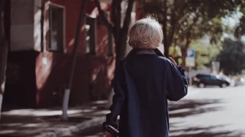 An Attractive Young Woman in a Blue Coat Walks Down the Street Turns with Loose Hair