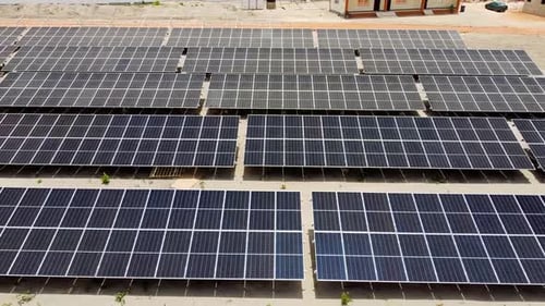 Basse aérienne glissant vers la gauche montrant des panneaux solaires bifaciaux poussiéreux et propres au NAWEC TBEA Jambur PV