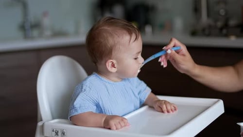 Donner à manger à un adorable bébé assis à table. Nourrir un mignon enfant calme à l'aide d'une cuillère à l'intérieur.