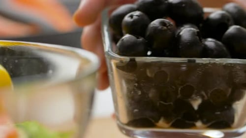 Pitted Black Olives Falling onto Light Wood Surface