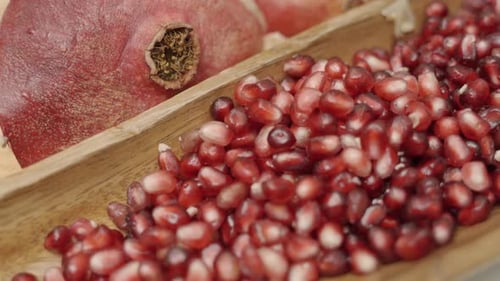 Close up panning shot of pomegranate seeds inside wooden plate juicing and using fresh ingredients a