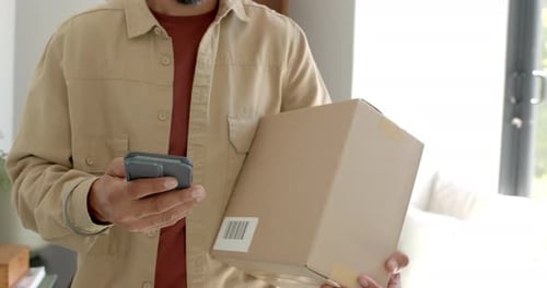 Holding smartphone, man carrying cardboard box and checking delivery details