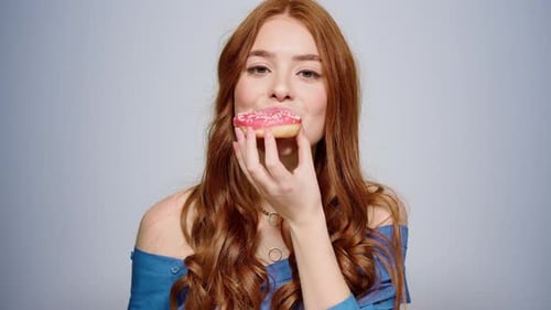 Red-haired Woman Bites Into a Pink Frosted Donut