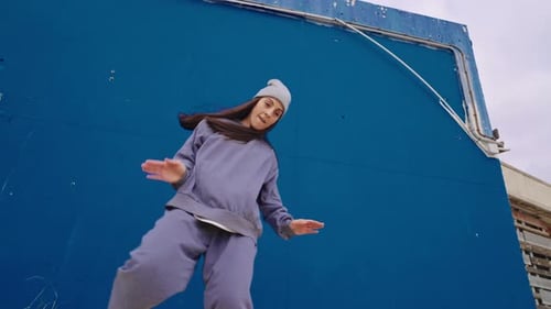 Woman Dancing Energetically Against Blue Urban Wall