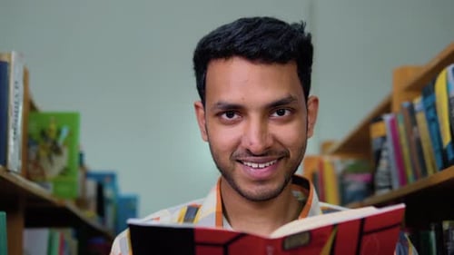 Happy Indian Male Student Reading a Book in the Library