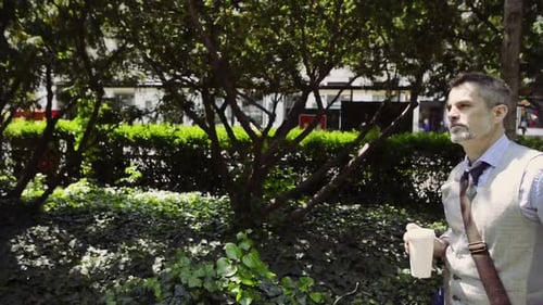 Mature businessman enjoying morning coffee during sunny walk in city park