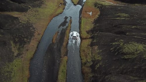 SUV-Crossover-Fahrzeug im flachen Fluss, das auf schlammigen Straßen in der atemberaubenden Landschaft Islands weiter fährt