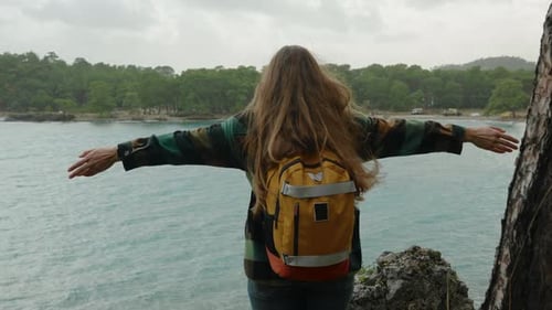 A lone woman traveler, with outstretched arms, feels free on a high cliff by the sea.