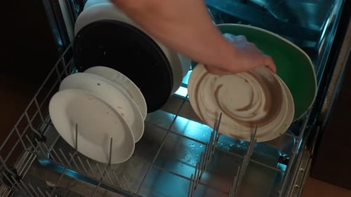 Closeup Highangle View of Unrecognizable Man Loading Backlit Dishwasher Machine with Dirty Dish and