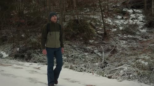 Male tourist in hiking sportswear with backpack walking in snowy forest