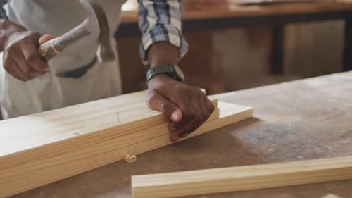 Mid section of african american male carpenter hammering nails into the wood at a carpentry shop