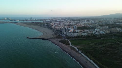 Aerial view of a city buildings in front of the beach with a bird passing in front of the camera
