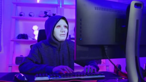 Masked person typing at neon-lit computer desk