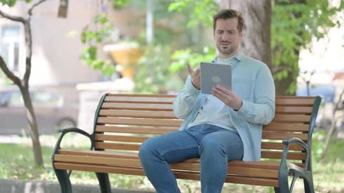 Man Using Tablet on Park Bench Chatting