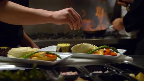 Chef plating food in restaurant kitchen with fire