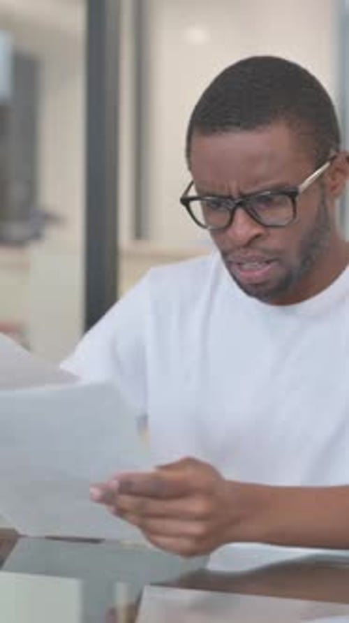 Concerned Man Reads Document at Table Indoors