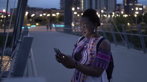 Stylish young woman using smart phone on city bridge at night portrait