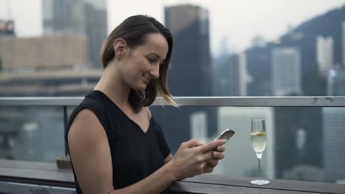 Young woman texting on smartphone and drinking champagne in luxury city skybar