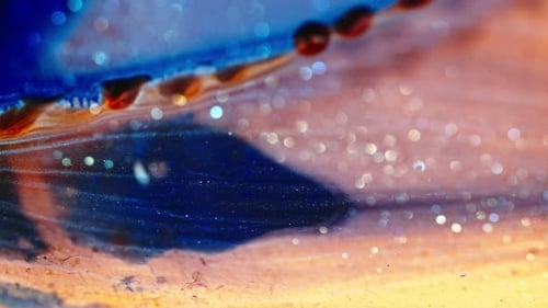 Swirling colorful liquids blend together with glittering particles in a view, abstract shot