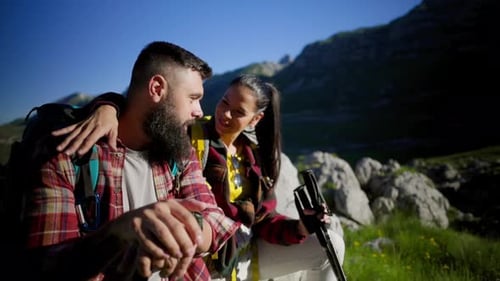 Hiking couple resting on mountain summit, enjoying panoramic valley view, talking and gesturing towa