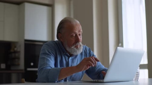 Senior Man Uses Laptop at Table