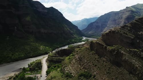 Majestic Mountainous Landscape with Winding River and Asphalt Road Under a Bright Sky