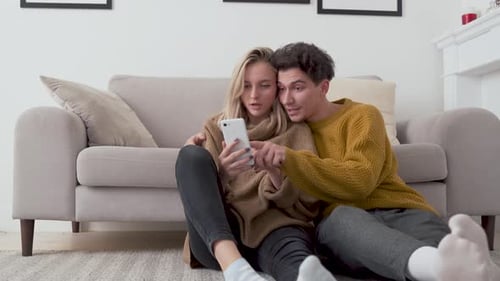 Couple Relaxing at Home Looking at Smartphone Together