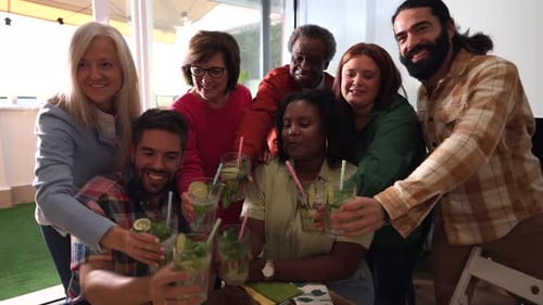 Multiethnic group of friends in their 30s enjoys making a toast while holding cocktails. Smiling and