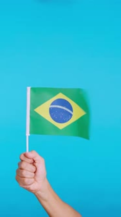 Hand hebt einen brasilianischen Wimpel, während er im Wind winkt