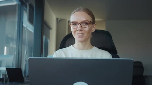 Focused Female Employee Wearing Glasses Working on Laptop in Bright Modern Office Demonstrating